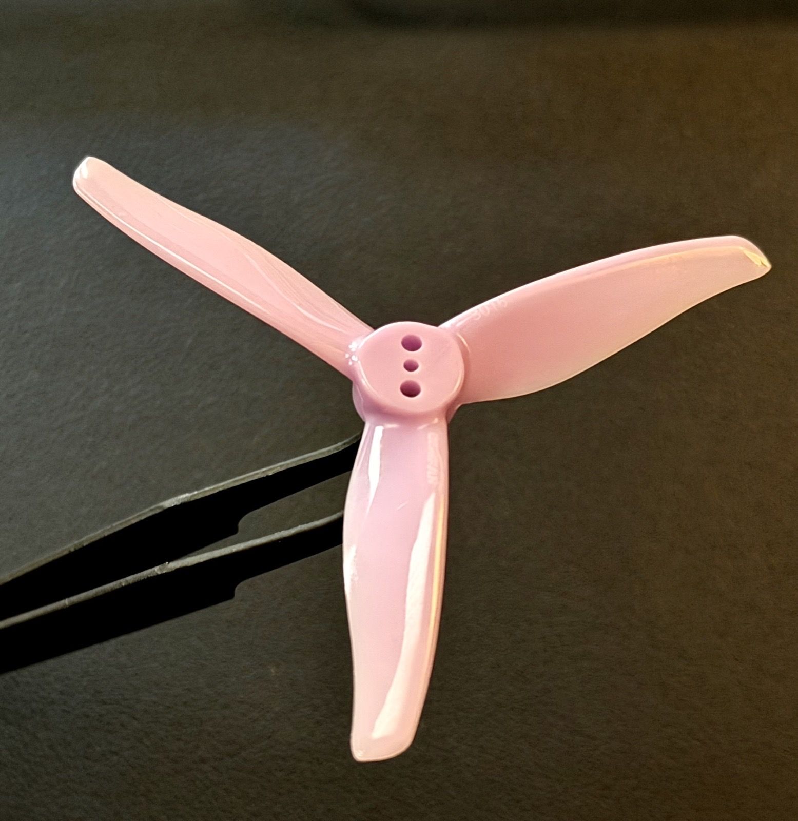 The real pink Gemfan Hurricane 3016 three-blade 3-inch propeller resting on a dark surface